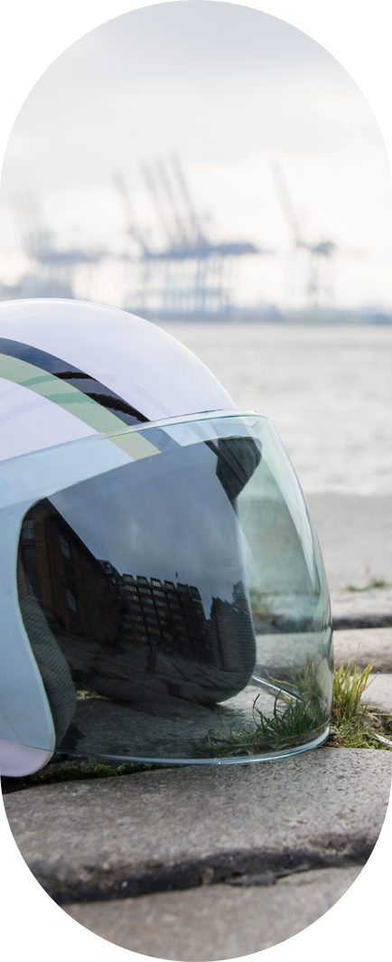Weißer Astronautenhelm liegt auf Pflastersteinen. Im Hintergrund der Hafen von Hamburg.