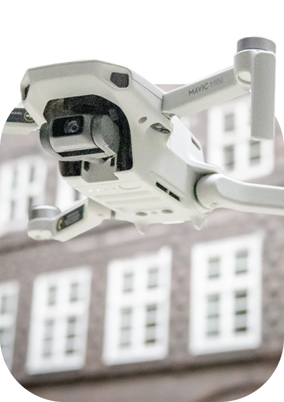 Fliegende weiße Drohne vor Hauswand. Die Drohne ragt etwas aus dem Bild heraus.