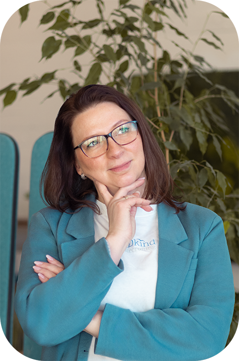 Nina in Denkerpose mit einer Hand am Kinn und grübelndem Blick zur Seite. Sie trägt ein weißes T-Shirt mit blauem Blazer darüber und eine Brille.