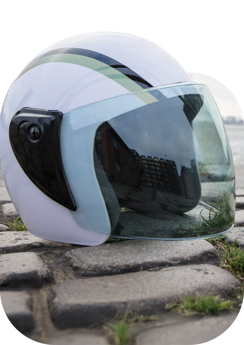 Weißer Astronautenhelm liegt auf Pflastersteinen. Im Hintergrund der Hafen von Hamburg. Der Helm ragt etwas aus dem Bild heraus.